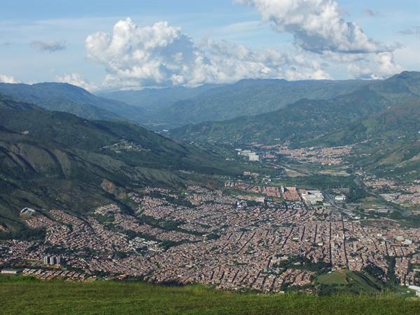 City among green mountains, dense rooftops under white clouds and blue sky
