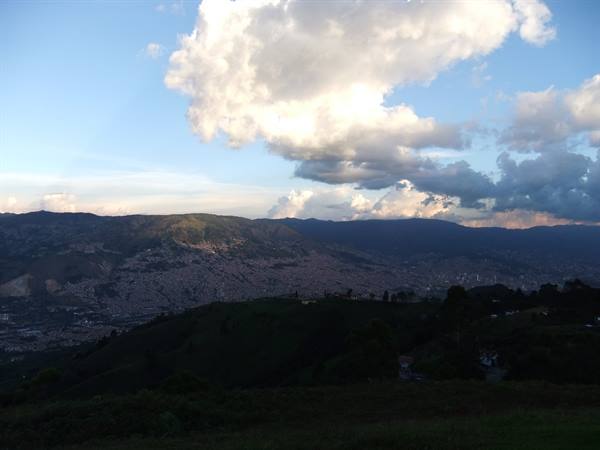 Sunlit clouds above Medellín valley, green hillside in the foreground