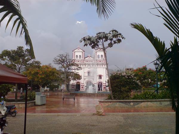 White and red church with fountain, rain-soaked square framed by palms