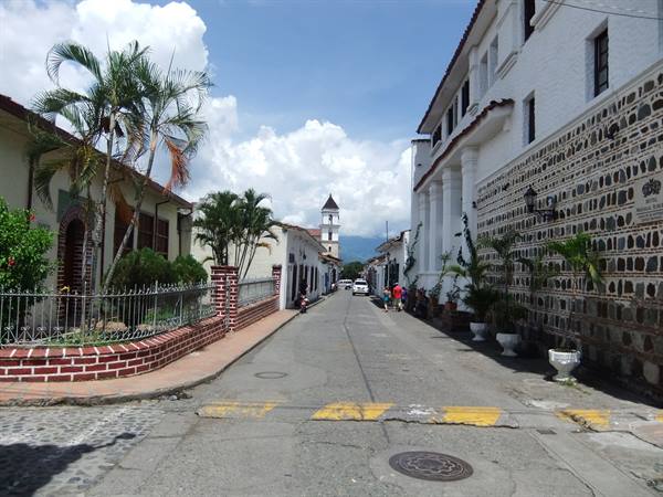 Cobblestone street with white colonial houses, palm trees and church tower ahead
