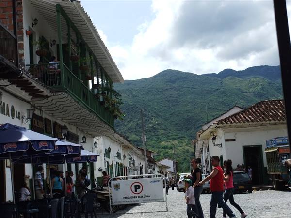 People walk the cobblestone street of Jardín among green wooden balconies and mountains