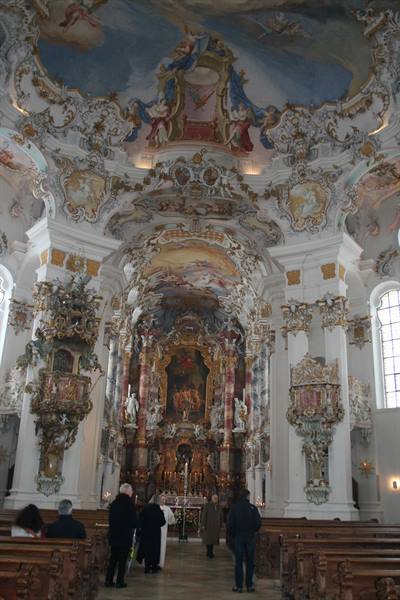 Baroque interior of the Wieskirche, gilded altar, frescoed ceiling and visitors among pews