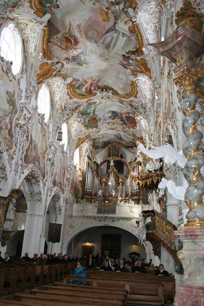 Baroque interior of Wieskirche: vault frescoes, gilded organ and visitors in pews