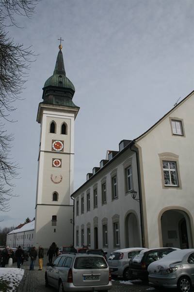 White church tower with clock and green dome beside a building, snowed cars
