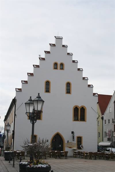 White stepped-gable building with arched windows, outdoor café tables and street lamps