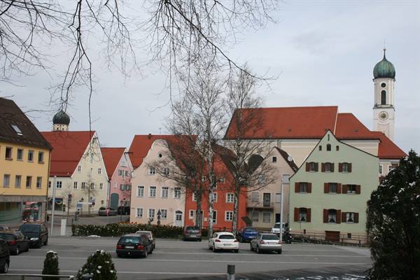 Colorful houses with red roofs and a green-domed church tower under grey sky