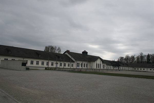 White barracks and gravel courtyard of the Dachau memorial under cloudy skies