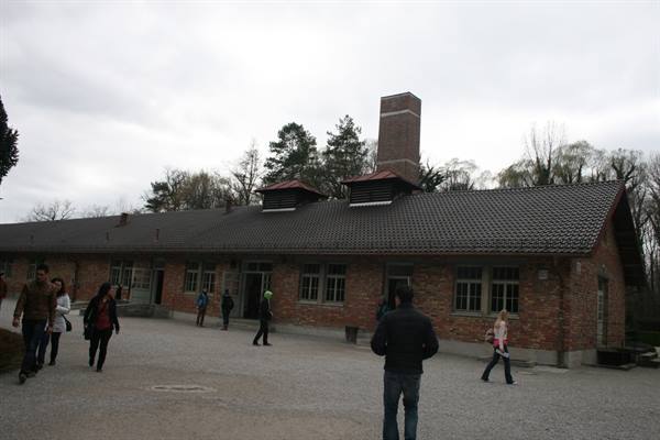 Visitors walking past the brick crematorium building at Dachau memorial, grey sky