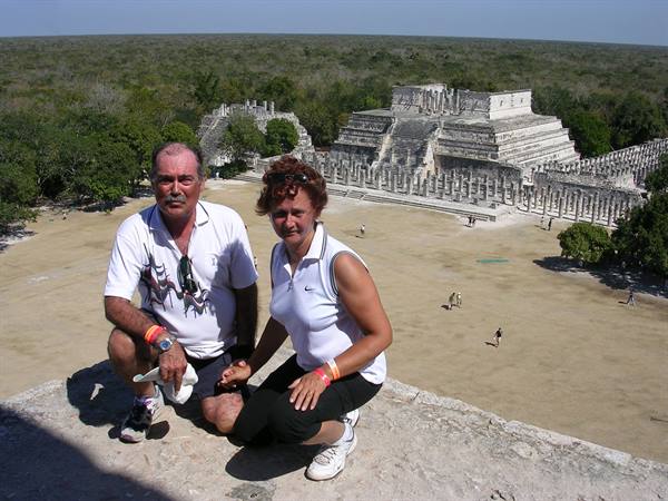 Couple posing atop Chichen Itza, Temple of Warriors in bright sunlight behind