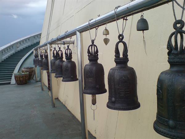 Bronze temple bells hanging from a metal beam beside a staircase