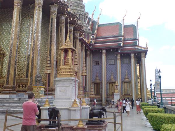 Tourist photographs bronze elephants in front of gilded temple at Bangkok Grand Palace