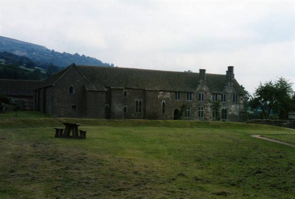 Old stone manor house with slate roof, green lawn and wooden picnic table in front