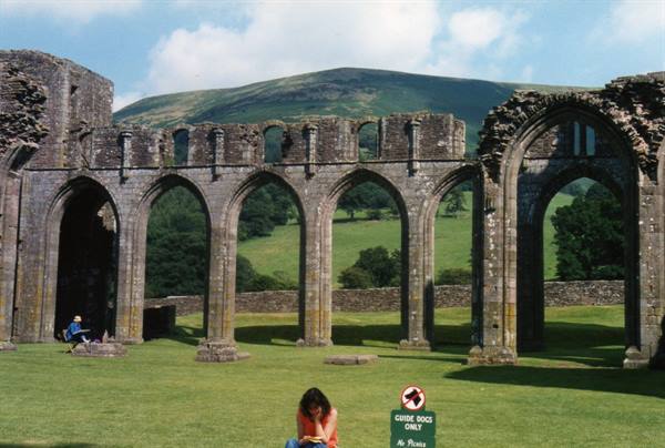 Tourist sitting on the lawn before Llanthony Priory's medieval stone arches