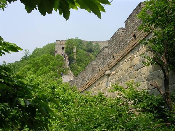Stone walls of the Great Wall amid greenery, tourists climbing the steps