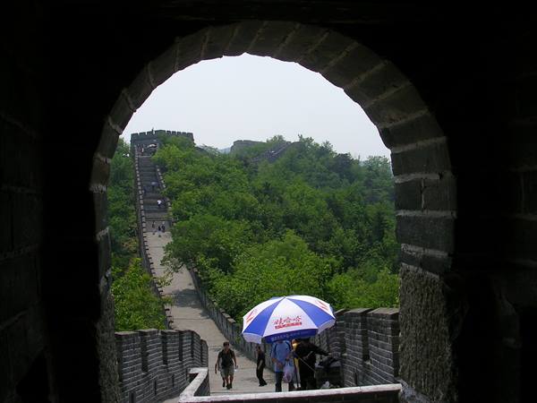 Tourists with blue umbrella under the stone archway of the Great Wall