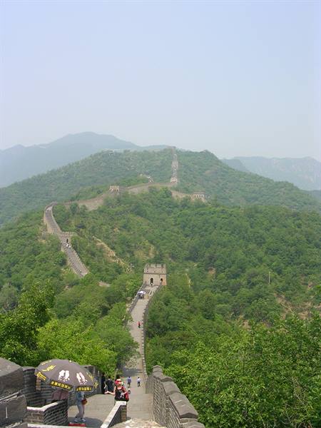 Tourists with umbrella climb the Great Wall between stone towers and green hills