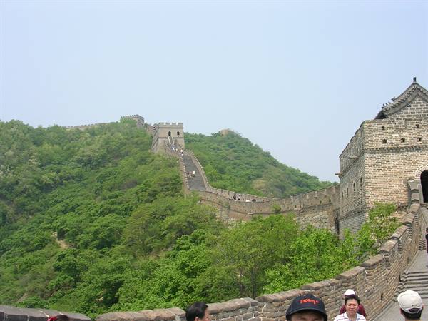 Tourists walk along the stone Great Wall of China winding over green hills