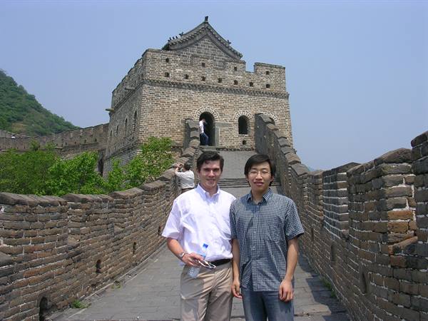 Two tourists pose in front of a stone watchtower on the Great Wall