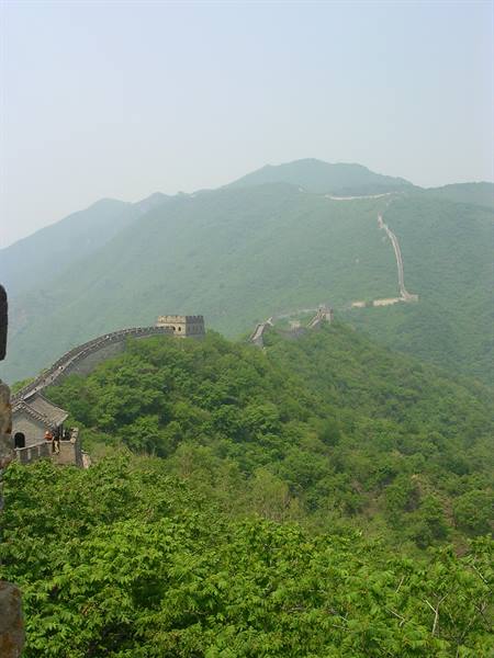 The Great Wall of stone winds over green hills under hazy sky
