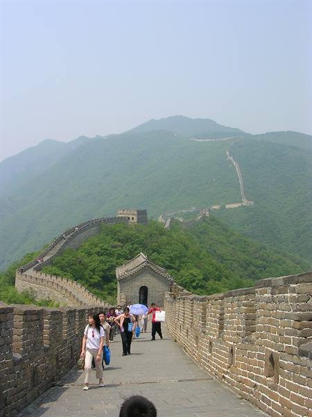 Tourists walk along the brick Great Wall winding through green mountains at Mutianyu