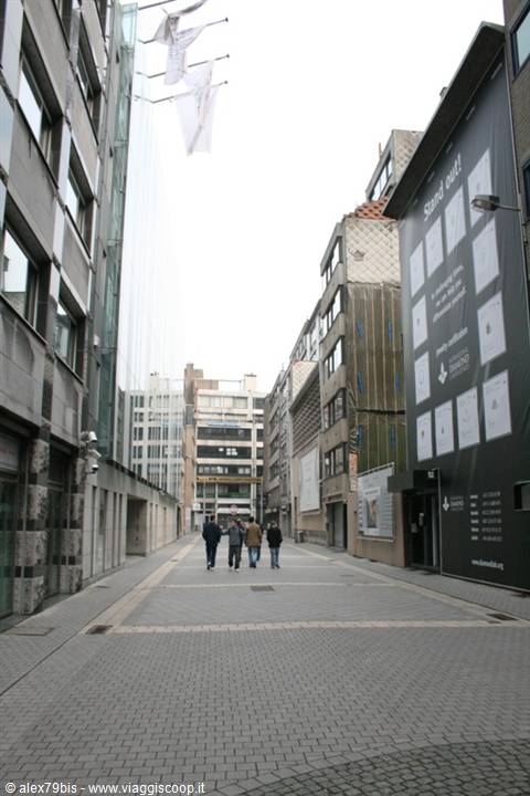 Pedestrians walk along a paved street between modern buildings with white flags