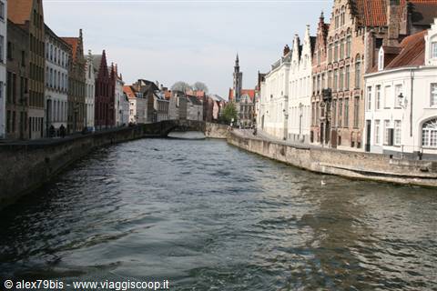 Bruges canal flanked by brick houses, stone bridge and belfry in the distance
