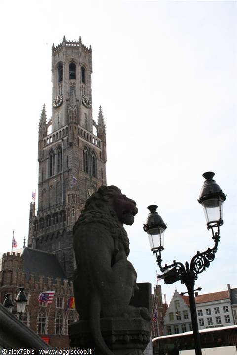 Stone lion statue in front of Bruges Belfry, wrought-iron lanterns, bright sky
