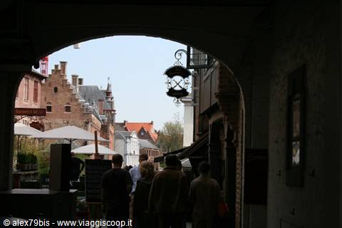 People under a dark archway look toward Bruges brick houses