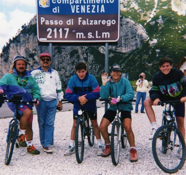 Cyclists posing with their bikes beneath the Passo di Falzarego sign at 2117 meters