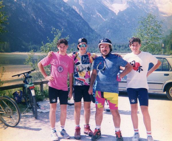 Four cyclists in 1990s gear pose with bikes by Lake Dobbiaco