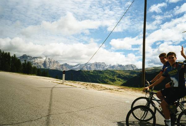 Two cyclists in blue jerseys ride uphill on asphalt road among Dolomite peaks
