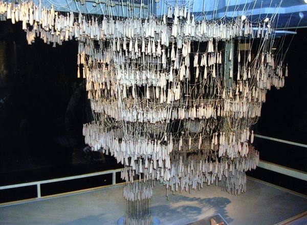 Installation of hundreds of small white figures hanging on wires, in a museum