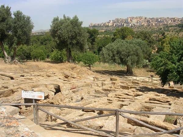 Rock-cut tombs carved in stone at Pantalica, wooden fence, olive trees, town in distance