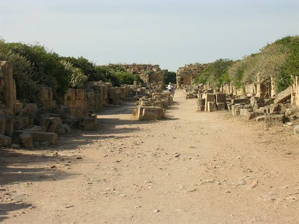 Visitors walk among ancient stone ruins along a dirt road, Cyrene