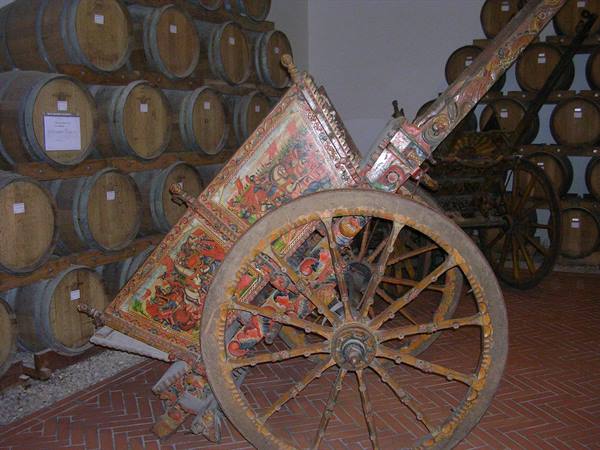 Painted Sicilian cart in cellar among wooden wine barrels