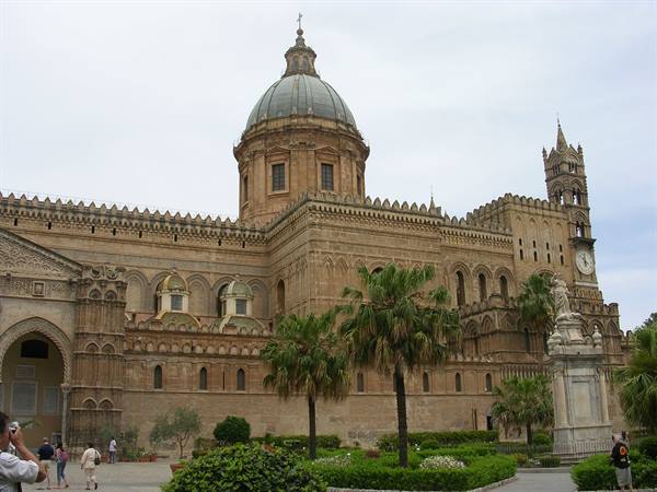 Tourists in front of Palermo Cathedral among palms and garden, soft light