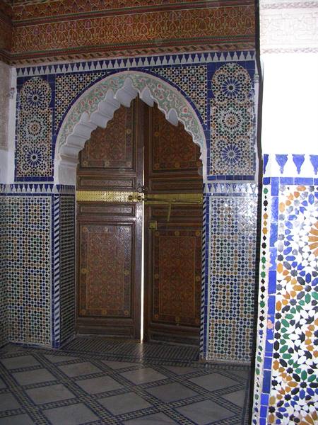 Carved wooden door beneath a scalloped arch, blue zellige tiles, Moroccan medina