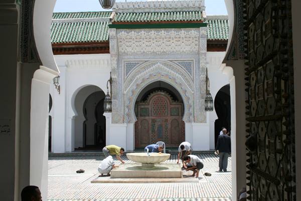 Men cleaning the fountain in a mosque courtyard with arches and zellige