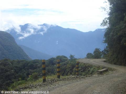 Dirt road with yellow and black posts among misty mountains and green forest