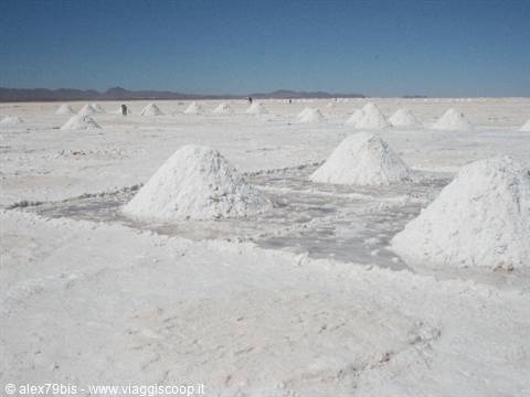 Conical white salt piles harvested on the salt flat, blue sky and distant mountains