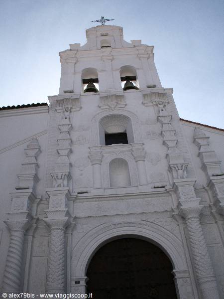 White baroque church facade with bell tower and bells against blue sky