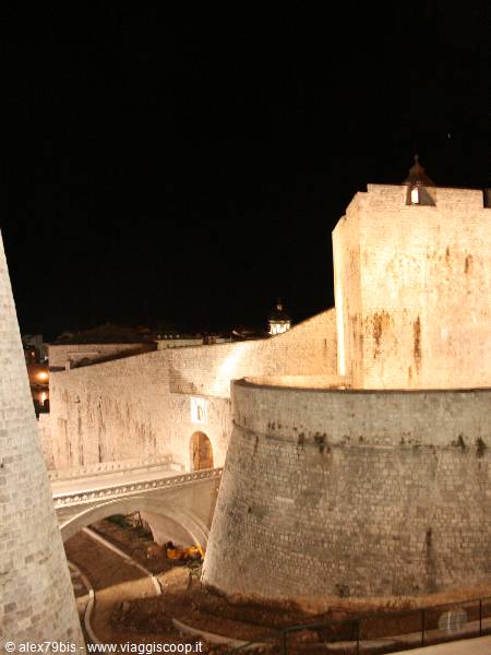 Dubrovnik stone walls lit at night, round fortress tower and entrance bridge