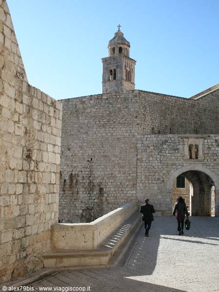 Tourists walk toward the stone gate beneath Dubrovnik's bell tower