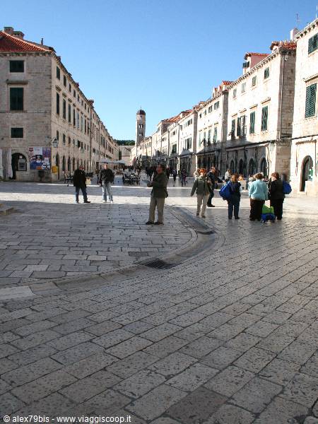 Tourists walk on Stradun's stone pavement in Dubrovnik under a blue sky