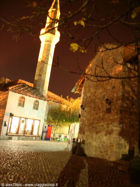Illuminated minaret at night above stone houses and cobblestones