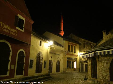cobblestone street at night, red-lit minaret, old stone facades