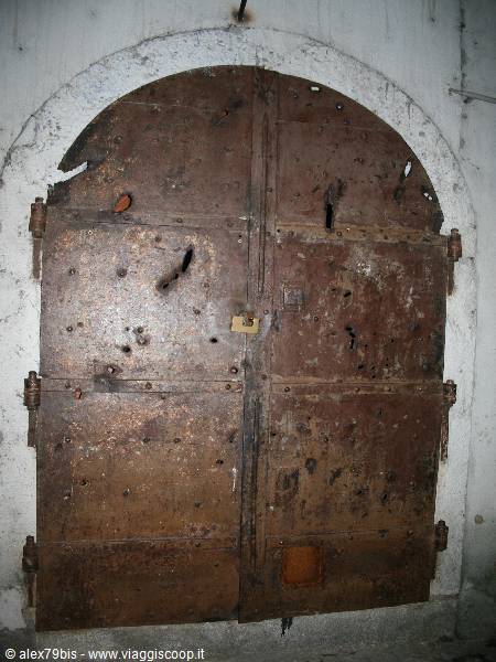 Old rusted iron studded door with padlock beneath a white archway