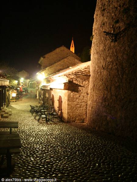 Night cobblestone alley, lit stone walls, glowing church bell tower