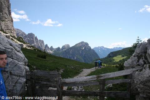 Hikers past a wooden fence between rock walls below the Dolomites