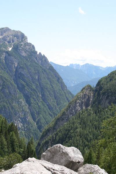 Grey boulders above a green forested valley and rocky peaks